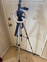 Full view of the Amazon Basics tripod with camera swivel head and a circular halo lighting lamp mounted on it near a door.
