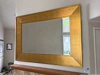 Full front view of large gold framed mirror hanging on a wall, showing the entire reflective surface and broad frame.