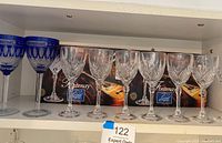 Seven clear diamond cut Fontenay crystal sherry wine glasses and two cobalt blue Somerset cut to clear crystal wine glasses shown on shelf with original Fontenay boxes behind the clear glasses.