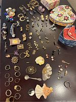 Full view of assortment of costume jewelry on table, showing earrings, rings, pins, button covers, and storage boxes.