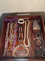 Full view of wooden tray containing multiple beaded necklaces and bracelets.