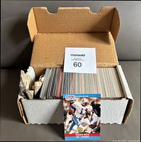 Wide view of the open box containing the football cards stacked neatly, front card shown is Warren Moon QB Oilers.
