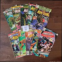 Lot of 10 Marvel comic books laid out on wood floor showing all covers visibly including The Man-Thing, The Sub-Mariner, Tomb of Dracula.