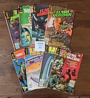 Lot of 8 Gold Key comic books laid out on a wooden floor showing various covers including Flash Gordon, UFO Flying Saucers, UFO & Outer Space, The Twilight Zone, and Paul Revere's Ride.