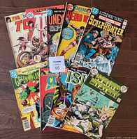 Photo showing all 9 comic books arranged on a wooden floor displaying front covers including Tor #1 and #2, Unexpected, Weird Worlds, Scalphunter, Green Lantern, Claw the Unconquered, The Mighty Isis, and Weird Mystery Tales
