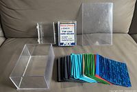 Full view of card collecting supplies showing the sealed pack of 25 top load card holders, clear plastic containers, and assorted colored soft sleeves laid out.