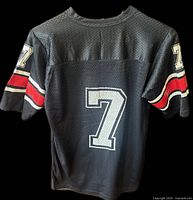 Rear view of black mesh jersey with large white number 7 and red and white sleeve stripes.