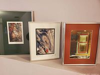 Three framed modern prints displayed side-by-side with different styles and matting colors, photographed to show all prints together.