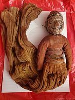 Full doll with wooden painted head and long cloth wrap laid on a red surface