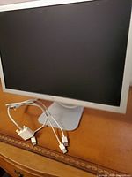 Front view of Apple monitor showing screen and cables on wooden surface.