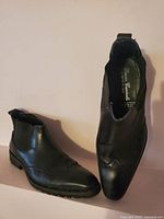 Top view of pair of men's black leather ankle boots showing pointed toe and brogue perforation detail.