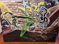 Front view of modern abstract painting on board showing stylized graffiti and two abstract human figures against a brick wall background.