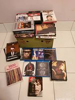 Stack of DVD and Blu-ray movies arranged on and around a green box, showing cover art for several films and two books. Includes recognizable titles and the condition of items can be visually inspected.