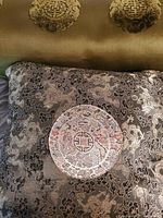 Close-up photo of one pillow showing dark silky fabric with detailed embroidered medallion pattern in the center, including intricate floral and oriental motifs