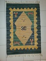 Image of a small vintage hand knotted rug with a central tan diamond and geometric motifs in green, yellow, and red hues, showing fringed edges and signs of age wear.
