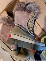 Photo of side view of one brown Sorel winter boot with fur around the cuff and green rubber sole.