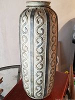 Full view of the tall ceramic vase showing vertical scroll design panels on its body.