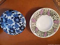 Two vintage porcelain plates, one with blue floral pattern and one with purple thistle design