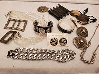 Various vintage costume jewelry items laid out showing necklaces, bracelets, earrings, brooches, belt buckles, and hair combs.