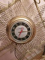 Full view of vintage Mastercrafters starburst style wall clock with visible electrical cord and aged brass finish.