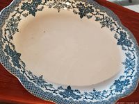Top view of vintage oval ceramic platter with blue floral and leaf design on edge, white center, minor surface marks.