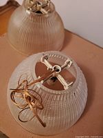 Two slightly yellow tinted Holophane crystal lamp globes with textured ribbed and crosshatch patterns, showing metal mounting hardware inside with attached brass wiring.