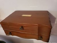 Closed vintage wooden jewelry box with three brass-colored clasps and a metal plaque on top.