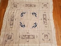 Full view of vintage linen fabric with hand sewn grid lines and multiple embroidered motifs including birds and rectangular floral patterns.