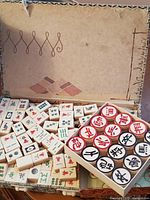 Photo showing Mahjong tiles with various Chinese characters and symbols, with checkers pieces including circular discs with red and black characters in tray.