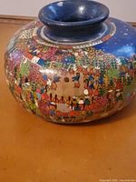 Close-up of the pottery vase's painted folk art scene showing groups of people and floral elements with a blue neck and rim.