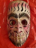 Front view of carved wooden mask with red and black paint detail, showing facial features and holes for eyes