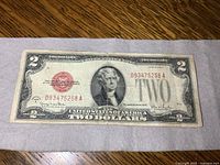 Front side view of a 1928 series US $2 bill laid flat on a wooden surface. Shows the full bill including serial number and red treasury seal.