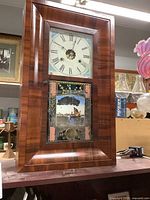 Front view of the wooden ogee style clock showing clock face and reverse painted glass nautical scene