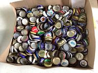 Tray containing a large quantity of assorted metal bottle caps with different brand logos and colors, showing special edition types.
