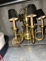 Close-up image showing the brass hanging light fixture with four lamp arms each topped with black fabric shades, placed on a metal surface.