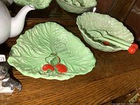 Shows Carlton Ware green leaf-shaped dishes placed on wooden surface, including a triangular plate with cherry motif and a salad bowl with matching spoons.