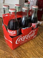 Cardboard case with six 8 oz Coca-Cola glass bottles with red and white caps, showing classic branding and vibrant vintage labels.