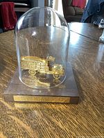 Gold colored Coca Cola delivery truck under clear glass dome mounted on wood base with plaque