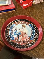 Top view showing the whole Coca-Cola tray on wood surface, including the red rim and vintage lady artwork.
