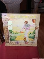 Front cover of the Goodbye Yellow Brick Road album showing colorful illustration of Elton John and yellow brick road.