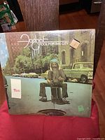 Front cover of Foghat Fool for the City vinyl LP album showing a man sitting on a manhole cover with city street and vintage cars in the background.