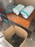 Four rolled horse saddle pads resting on a wooden chest next to a box containing a dark-colored horse bridle or harness with multiple straps and buckles