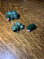 Top view of the three small green jade animal figures, showing a bear, a frog, and a turtle all placed on wood grain surface.