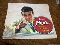 Full view of the Moxie cardboard display showing the entire man pointing and logo with visible creases and stained corner