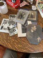 Collection of several old black and white photographs laid out on a wooden table showing various portraits of men in formal attire.