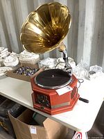 Front and side view of the radio showing wooden base, black turntable, brass horn, and attached power cord.