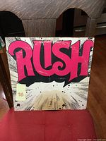 Front cover of Rush LP album featuring large pink 'RUSH' title and vintage design.