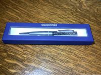 Silver-tone Swarovski pen with small silver crystals inside barrel, displayed in blue Swarovski box on wood surface.