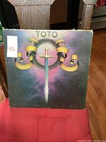 Front cover of the Toto LP album with sword and ribbon artwork and minor wear on edges.