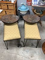 Pair of vintage metal framed end tables with oval faux marble tops and upholstered seats beneath, seen from front on concrete floor, showing matching design and metal legs.